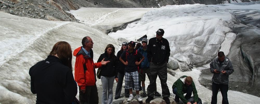 Male and female students standing on a glacier listening to a male professor's lecture