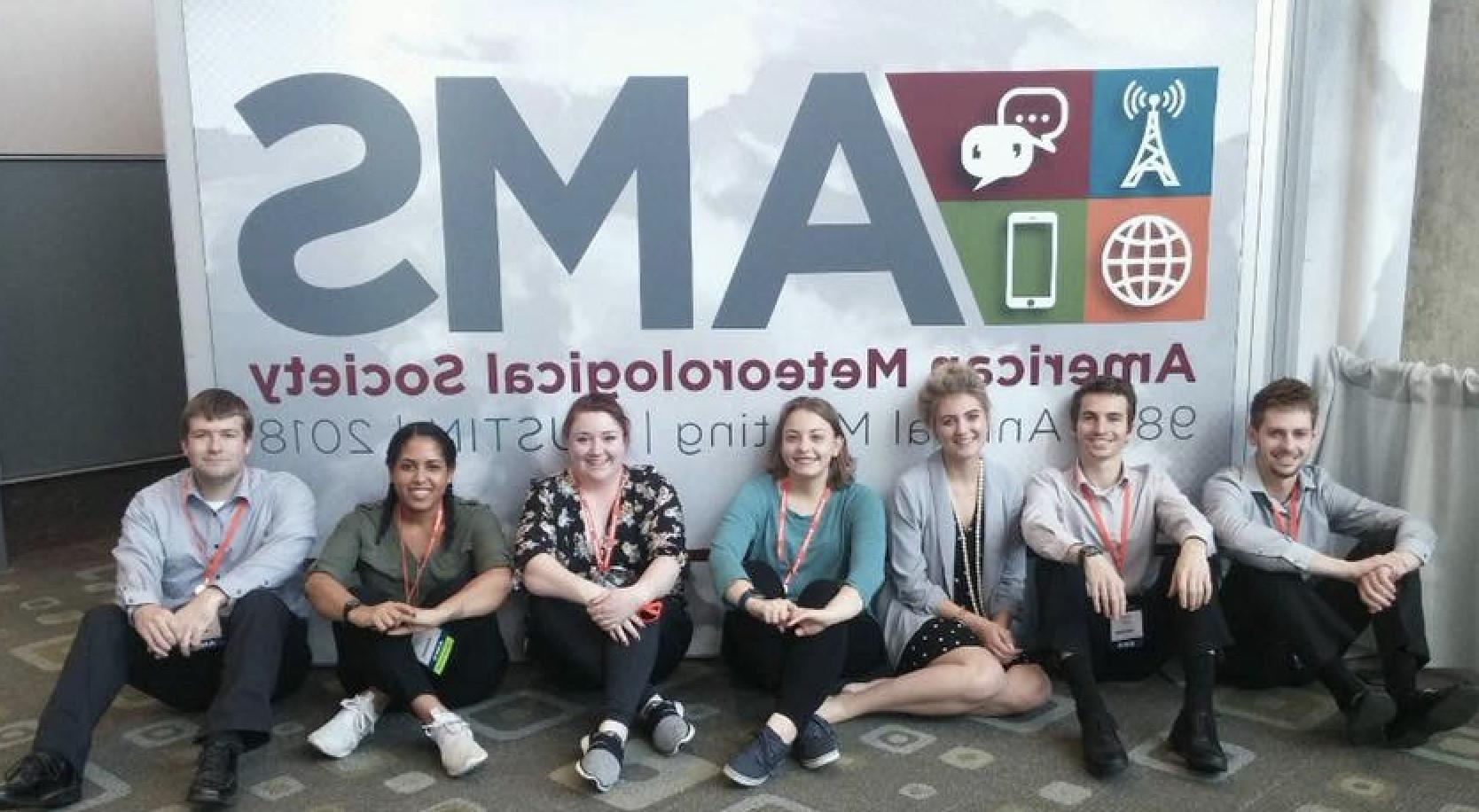 Students sitting in front of the AMS sign