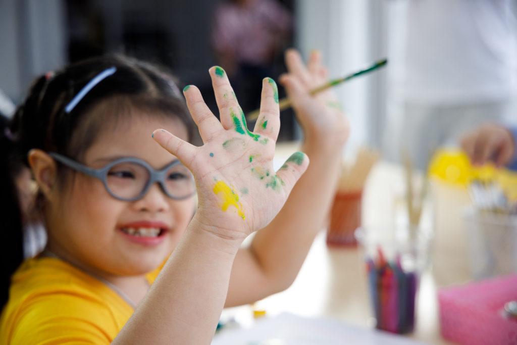 Happy Asian girl with Down's syndrome painting her hand with water color in art class.