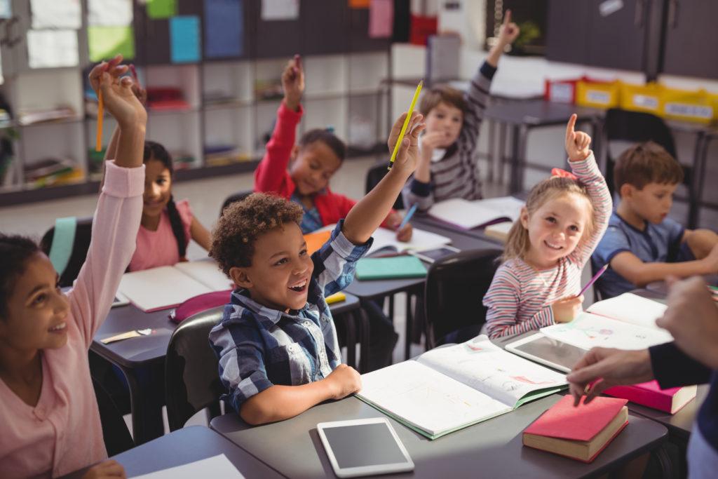 Schoolkids raising their hands in classroom at school