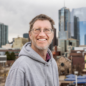 Dr. John Carter smiling with the Denver skyline behind him