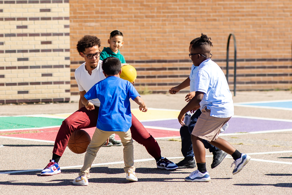 Photo of a MiSTER playing basketball with 4 kids outside.